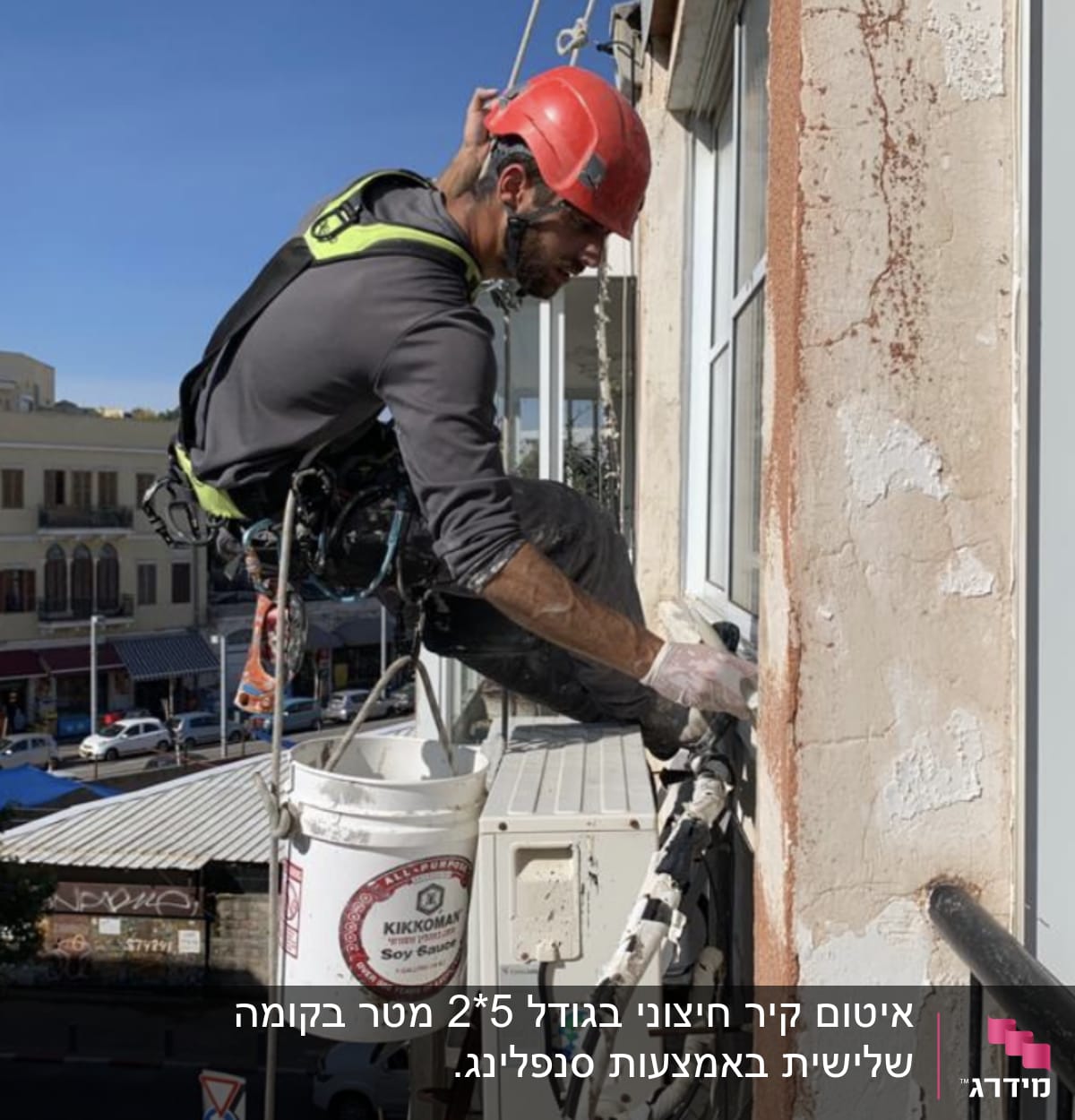 עובד בגובה עם קסדה אדומה מתקין מזגן על קיר חיצוני